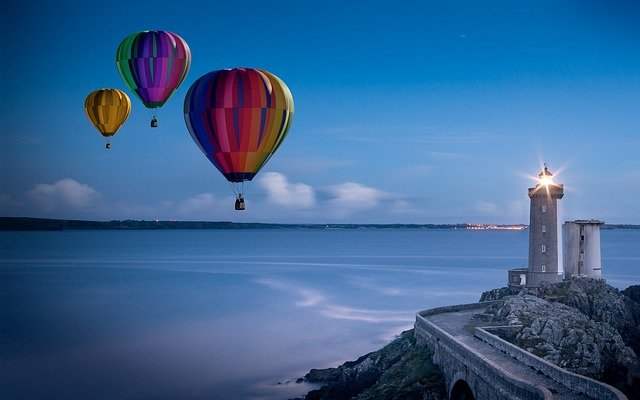 Hot air baloons floating over the ocean near a light house